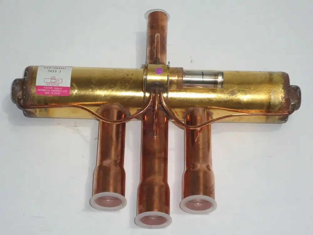 4-Wege-Ventil von Daikin mit einem zentralen Gehäuse und drei Ausgangsrohren. Sichtbares Etikett auf der Seite. Metallische Oberfläche und Wärmeleitfähigkeit erkennbar.